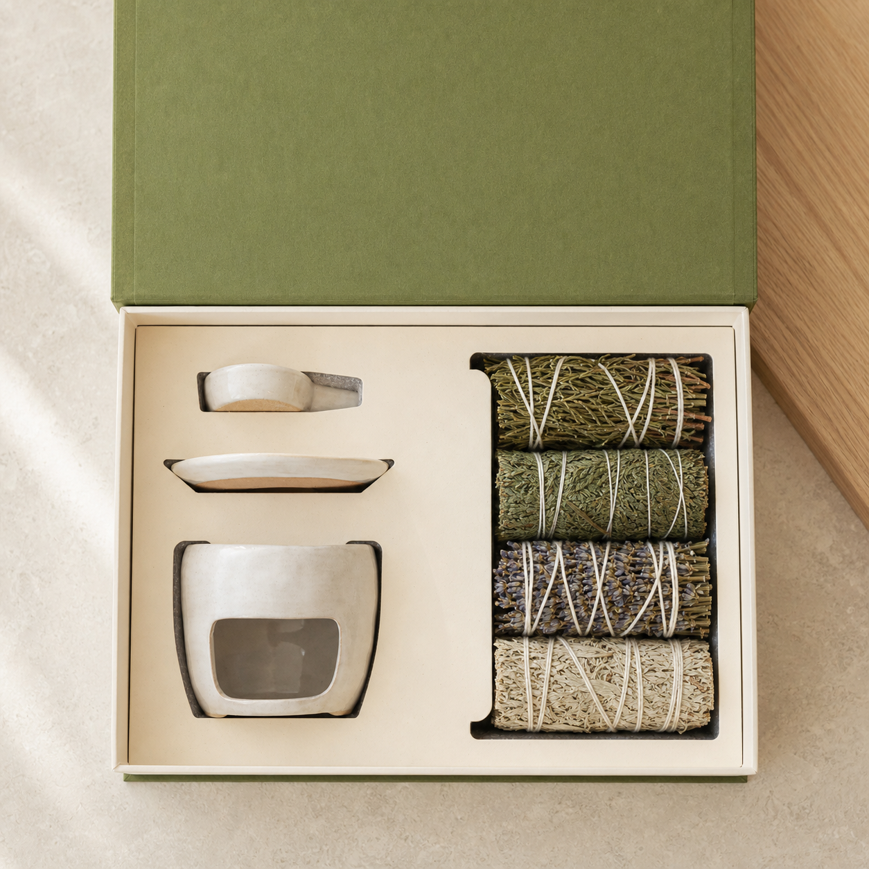 Top view of an open gift box with a white ritual vessel and four tied botanical bundles