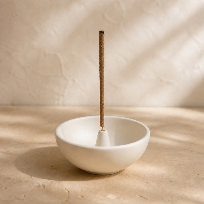 White bowl-shaped incense holder with one upright incense stick