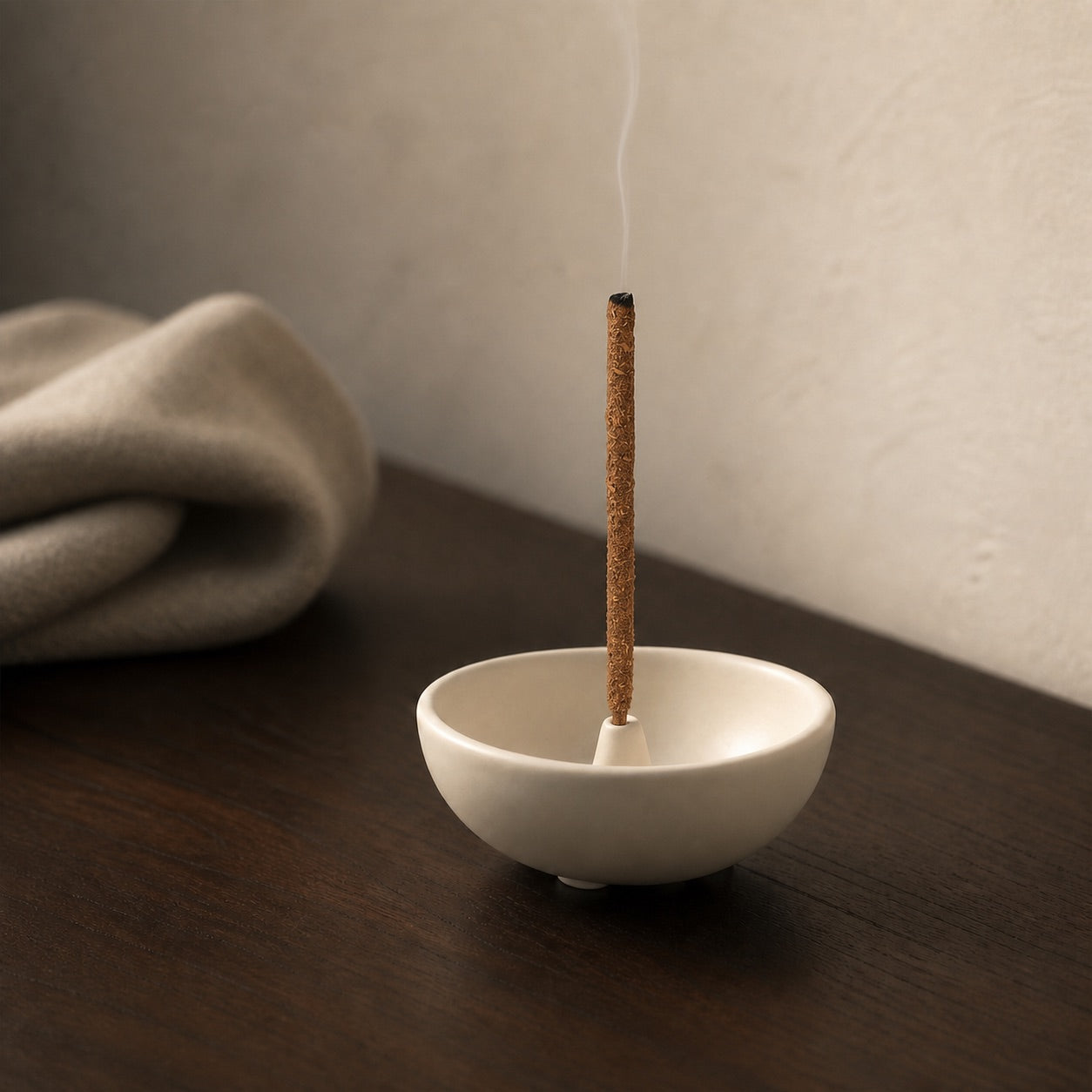 Lit incense stick in a white bowl-shaped holder on a dark surface