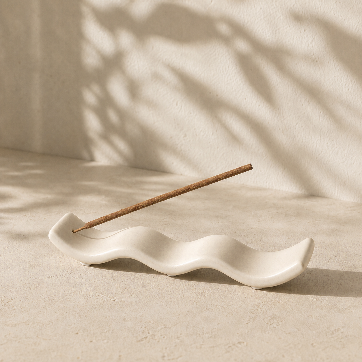 White wave-shaped incense holder with one incense stick in a neutral setting