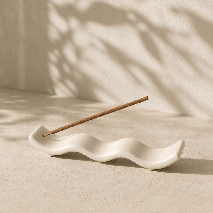White wave-shaped incense holder with one incense stick in a neutral setting