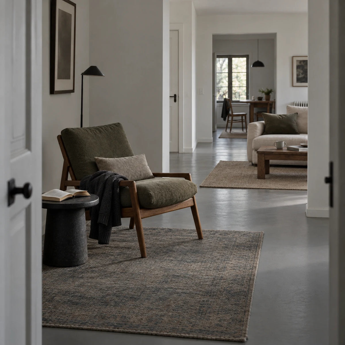 A reading chair with a cardigan and open book connects to a sitting room and dining space beyond.